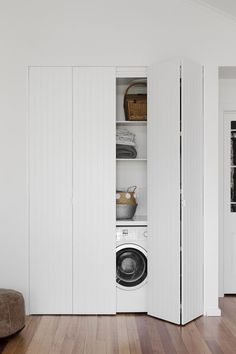 a washer sitting inside of a white closet next to a wooden floor in a room