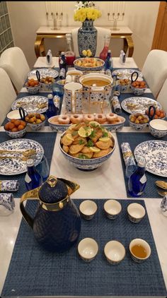 a blue and white table set with plates, bowls, cups and teapots