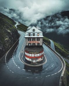 an old building on the side of a road in the middle of mountains and clouds