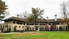 a large house with lots of windows and trees in the front yard, surrounded by lush green grass