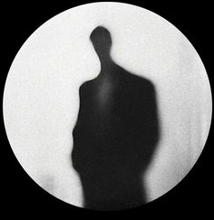 a black and white photo of a man's shadow in front of a circular object