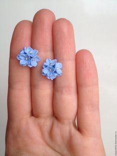 two tiny blue flowers are sitting on someone's hand and they look like they have been made out of polymer