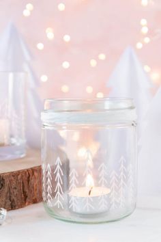 a glass jar with a candle inside sitting on a table next to a piece of wood