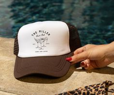 a woman's hand holding onto a trucker hat next to a swimming pool