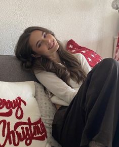 a woman sitting on top of a couch next to a pillow with merry christmas written on it