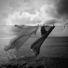 clothes hanging on a line over the ocean with cloudy skies in the background, black and white photograph