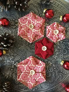 three red and white ornaments sitting on top of a metal tray next to pine cones