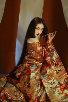 a woman in a kimono is holding a stick and looking at the camera while sitting down