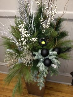 a vase filled with white flowers and greenery on top of a wooden floor next to a wall