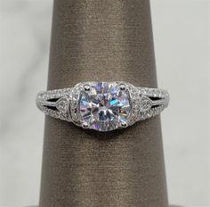 This Vintage Diamond Mounting Ring will be a show stopper! Ring is setup to hold a round cut Cubic Zirconium weighing approximately 1.00 ct. Mounting features 0.50ctw Round cut Diamonds, with G/H in color and SI1 in clarity. Ask a Sales Associate today to show you Featuring diamonds for this ring. All of our rings can be designed for different Shapes and Sizes featured stone. Moissanite Cluster Ring With Vs Clarity In Round Cut, Vs Clarity Diamond Cluster Ring Round Cut, Diamond White Halo Ring With Round Cut, Platinum Cluster Ring With Vs Clarity, Gia Certified Round Cut Halo Ring For Promise, Platinum Diamond Ring With Vs Clarity, Gia Certified White Gold Cluster Ring With Round Cut, Gia Certified Cubic Zirconia Cluster Ring, Diamond Halo Ring With Vs Clarity