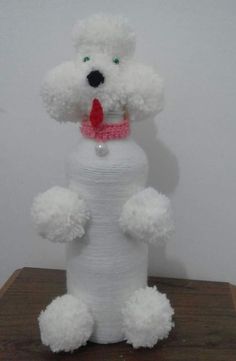 a white teddy bear made out of yarn on a wooden table next to a wall