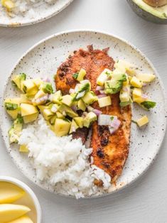 two plates with fish, rice and pineapple salsa on them next to sliced bananas