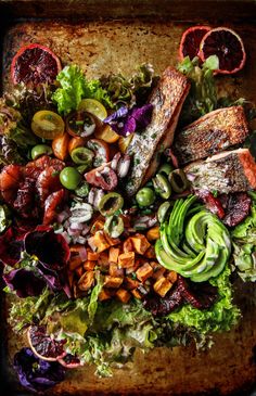 an overhead view of a salad with salmon and avocado on it, surrounded by oranges