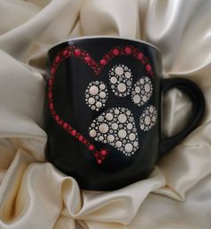 a black coffee mug with red and white designs on it's side sitting on a bed