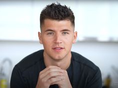 a close up of a person wearing a black shirt and holding his hand to his chin