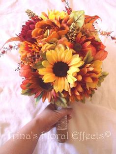 a bouquet of sunflowers and other flowers is being held by someone's hand