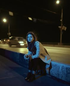 a woman sitting on the side of a road at night