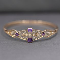 This pretty, lacy bangle is truly one of a kind. The center of the bracelet features two square cut bezel set amethysts, each about 0.33ct. They are matched by two smaller square amethysts set on point, each weighing approximately 0.10ct. Five seed pearls accent the bracelet but perhaps the main focus is the super intricate honeycomb structure of the top of the bangle. The bangle is nearly round and measures 2.5" across in diameter and is 2 3/8" tall inside. Across the top the bracelet measures Honeycomb Structure, Amethyst Set, Seed Pearl, Square Cut, Antique Victorian, Bezel Setting, Honeycomb, Seeds, Amethyst