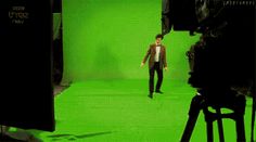 a man walking down a green carpeted floor in front of a camera set up