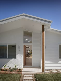 a small white house with an open front door and brick walkway leading to the entrance