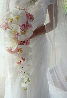 a woman in a wedding dress holding a bridal bouquet with orchids on it