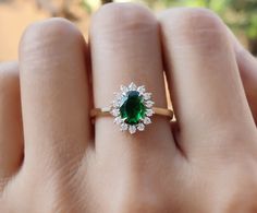 a woman's hand holding an emerald and diamond ring