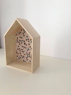 a small wooden house sitting on top of a white table next to a window with black triangles