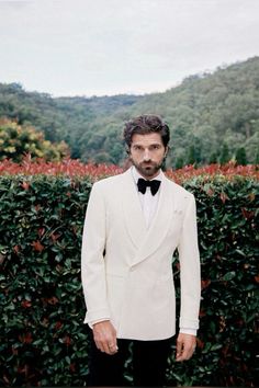 a man in a tuxedo standing next to a hedge