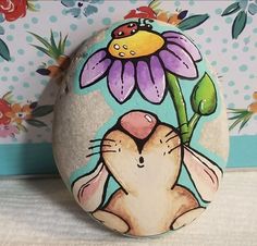 a painted rock with an image of a bunny holding a flower on it's face