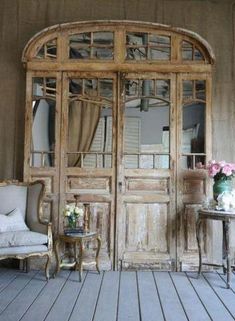 an old wooden room with two chairs and a table in front of the doors that lead to another room