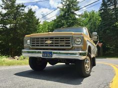 an old yellow truck is parked on the side of the road in front of some trees