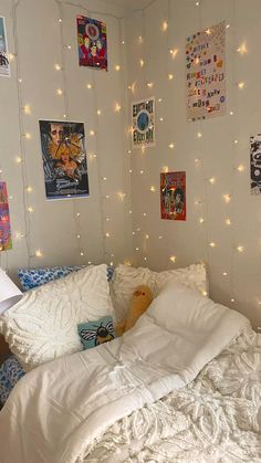 an unmade bed with white sheets and lights on the wall in a dorm room