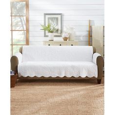 a white couch sitting in a living room next to a wooden table and dresser with a potted plant on top of it