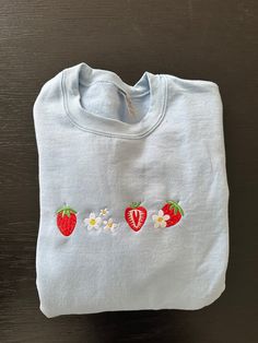 This girly trendy design features strawberries and flowers embroidered in the center with different strawberry phases. Strawberry crewneck is on a light blue crewneck and the flowers are white. Embroidery Inspiration On Clothes, Flower Clothes Aesthetic, Machine Embroidered Clothes, Strawberry Merch, Embroidery Designs Clothes, Cute Easy Outfits, Cute Crew Neck, Fruit Embroidery, Light Blue Crewneck