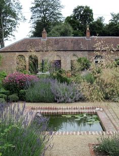 an old brick building with a pond in the middle and lots of plants around it