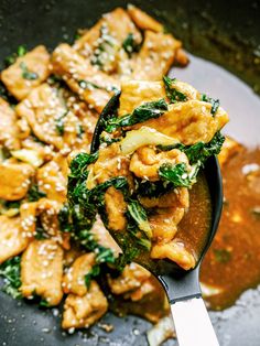 a spoon full of chicken and spinach stir frying in a skillet with broccoli