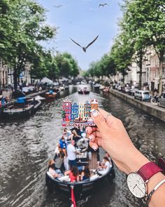 a person holding up a piece of paper with the word love spelled on it in front of a canal filled with boats