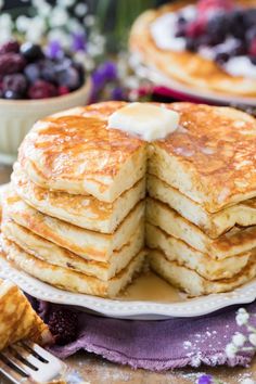 a stack of pancakes with butter on top and berries in the background next to them