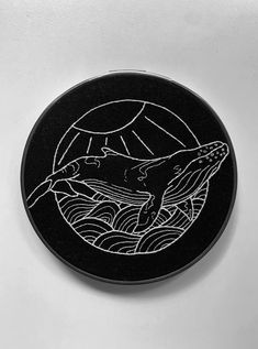 a black and white drawing of a whale on a round surface with waves in the background