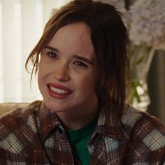 a close up of a person wearing a plaid shirt and smiling at the camera with flowers in the background