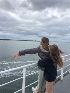 two people standing on a boat looking out at the water and clouds in the sky