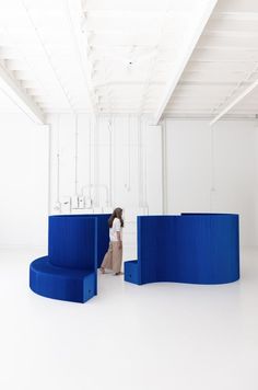 a woman is standing in the middle of a room with blue curved seating and white walls