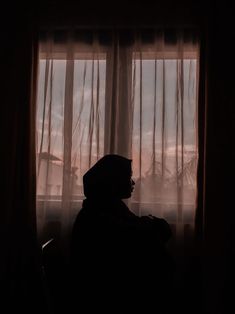 the silhouette of a person sitting in front of a window with sheer curtains on it