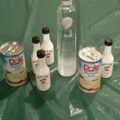 several bottles and cans of food sitting on a plastic tableclothed surface, with one empty bottle in the middle