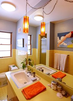 a bathroom with yellow walls and orange towels hanging from the ceiling, along with two sinks