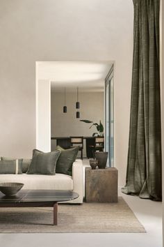 a living room filled with furniture next to a tall glass window covered in green curtains