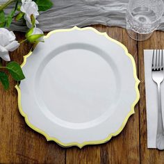 a white plate with yellow trim sits on a wooden table next to silverware and flowers