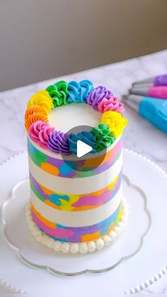 a rainbow cake with white frosting on a plate next to some scissors and markers