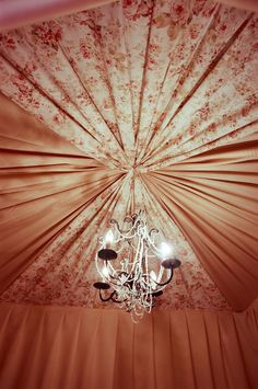 a chandelier hanging from the ceiling in a room with floral walls and curtains