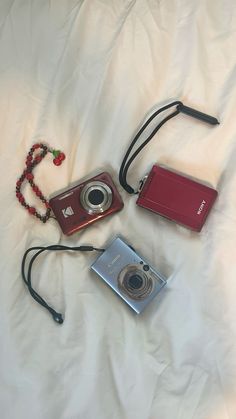 three different types of cameras laying on a white sheet with beaded necklaces and beads